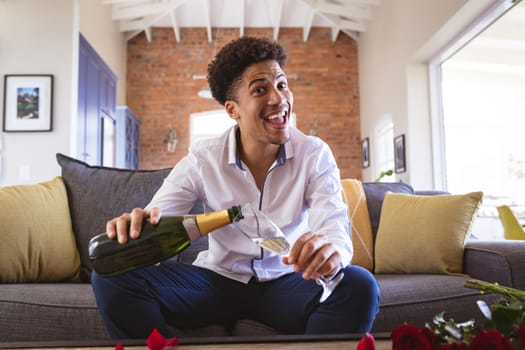 Cheerful young man pouring champagne in flute during virtual date from home. lifestyle and virtuality.