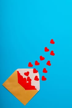 Overhead view of open beige envelope with red heart shapes by copy space over blue background. love and valentine present.