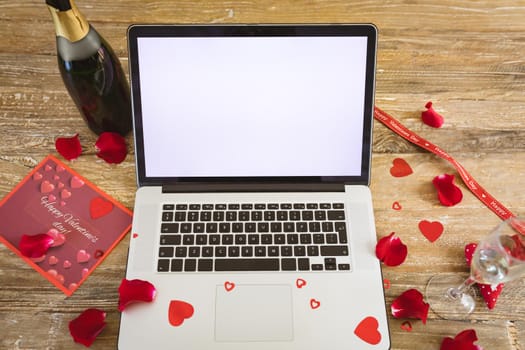 Blank screen on laptop with copy space by champagne bottle and rose petals on table. virtuality and telecommunications.