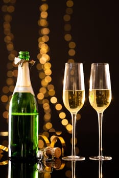 Open champagne bottle with flutes against illuminated lights against black background, copy space. drink, celebration and decoration.