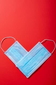 Overhead view of protective face masks arranged in heart shape on red background, copy space. valentine's day, covid-19 and illness prevention.