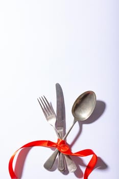 Overhead view of cutlery tied tightly with red ribbon below copy space over white background. valentine and dining.