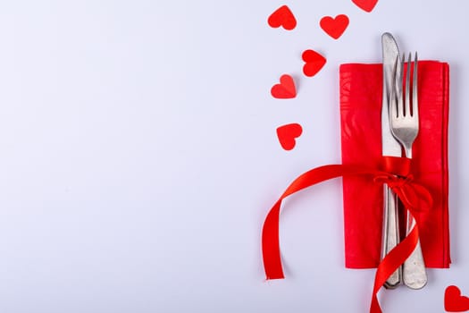 Overhead view of cutlery tied with red ribbon on napkin by copy space over white background. valentine and dining.