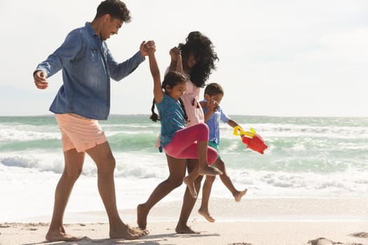 Playful multiracial family walking while holding hands on shore at beach enjoying sunny day. lifestyle and weekend.
