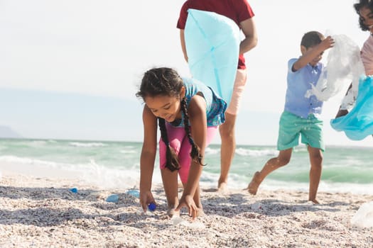 Biracial girl collecting plastic garbage on sand at beach with family during sunny day. lifestyle and environmentalism.