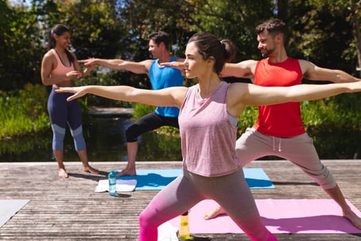 Female yoga instructor assisting men and woman during exercise session at park. healthy lifestyle and body care.