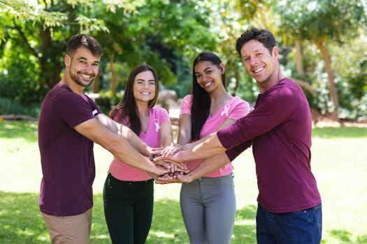 Portrait of happy multiracial friends stacking hands during breast cancer awareness campaign at park. breast cancer awareness campaign, friendship and unity concept.