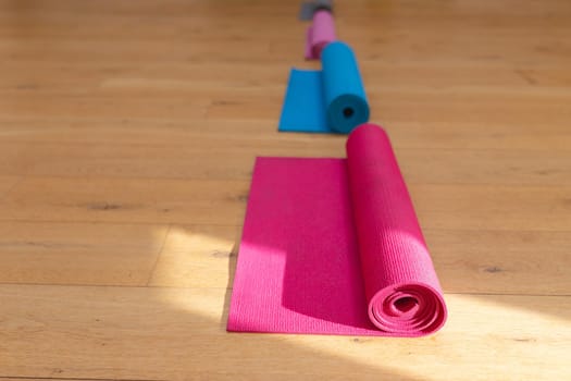 Rolled up exercise mats arranged in a row on hardwood floor in yoga studio, copy space. fitness, yoga and healthy lifestyle.