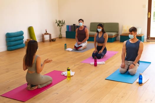 Female instructor with multiracial men and women wearing face masks in yoga studio during covid-19. new normal, illness prevention, pandemic and active lifestyle concept.