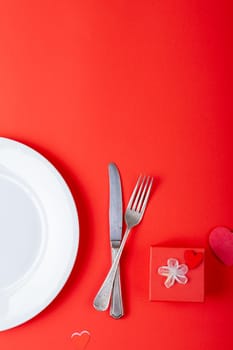 Overhead view of place setting by valentine gift on red background, copy space. valentine's day and love concept.
