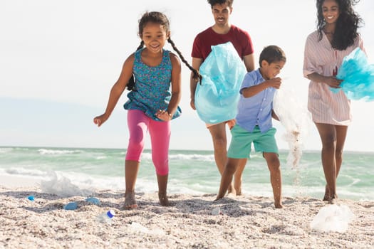 Happy responsible multiracial family collecting plastic garbage from sand at beach on sunny day. lifestyle and environmentalism.