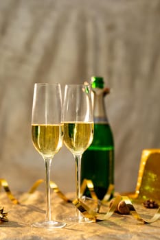 Closeup of champagne flutes by golden ribbon in front of bottle on table. celebration and party with copy space.