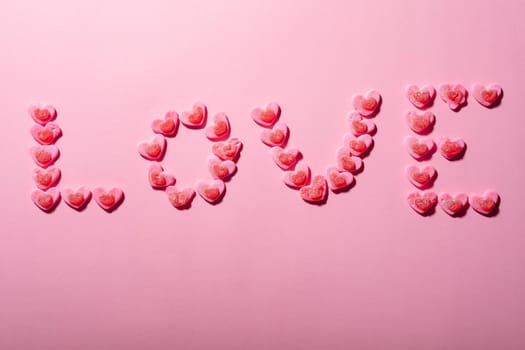 Love text made from heart shaped candies isolated on pink background, copy space. valentine's day, food and love concept.