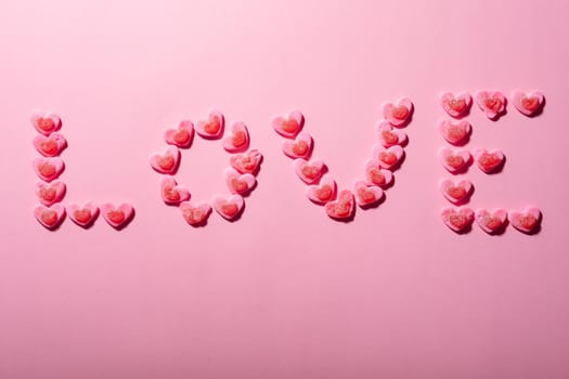Love text made from heart shaped candies isolated on pink background, copy space. valentine's day, food and love concept.
