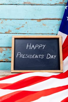 Happy presidents day text on writing slate with usa flag on blue wooden table with copy space. patriotism and identity, celebration.