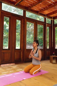 Biracial woman meditating while kneeling on exercise mat in yoga studio. healthy lifestyle, yoga and fitness.