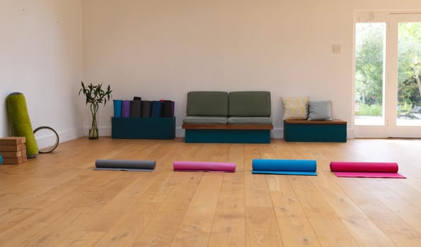Colorful rolled up exercise mats arranged side by side on hardwood floor in yoga studio, copy space. fitness, yoga and healthy lifestyle.