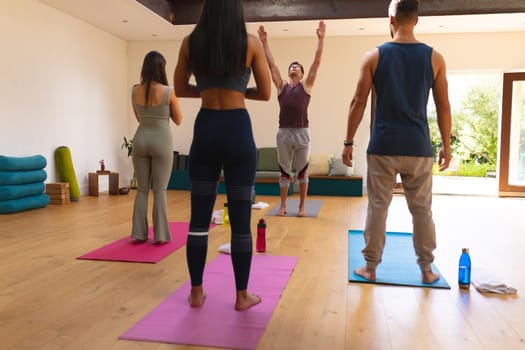Male instructor teaching yoga pose to multiracial man and women in yoga studio. fitness, yoga and healthy lifestyle.