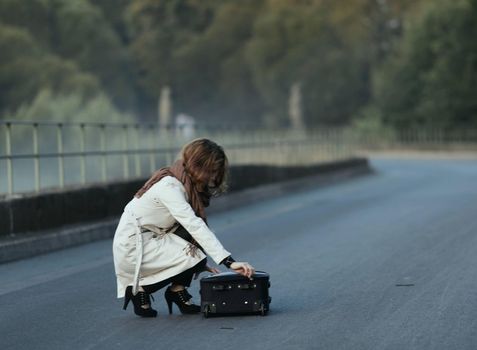 a dramatic moment in the life of the breakup of a relationship with a once loved one fleeing with one suitcase in the photo, the girl collects things in a suitcase in the middle of the roadway. High quality photo