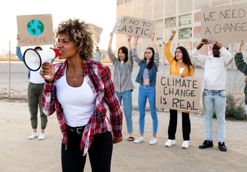 Young African American woman shouting through megaphone leading demonstration protesting against climate change and plastic pollution. Activism concept.