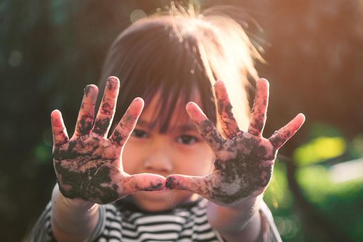 Cute little girl smiles and shows off her muddy hands while planting trees in the backyard. Educational concept outside the school fence.