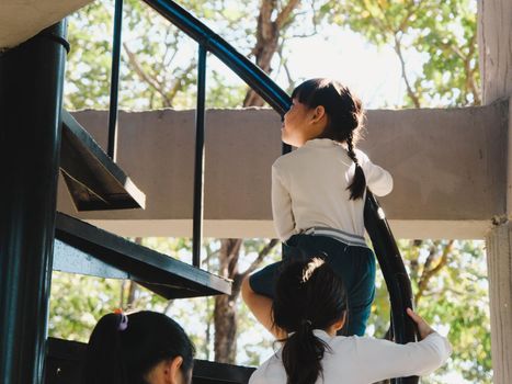 Mother helping daughter climb stairs to the tower in the playground. Family outdoor recreational activity.