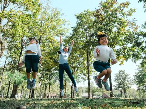 Two cute little Asian girls in summer outfits, having fun with a beautiful young mother smiling happily in the park. Motherhood and family concept.