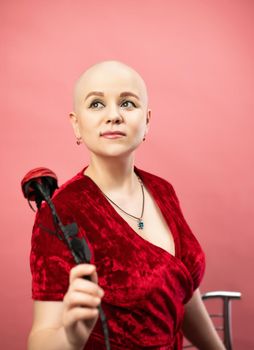 the portrait of a bald woman with cancer after chemotherapy in a red robe with an artificial rose flower