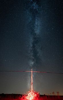 Power line and wooden pylon in bright burning red under milky way