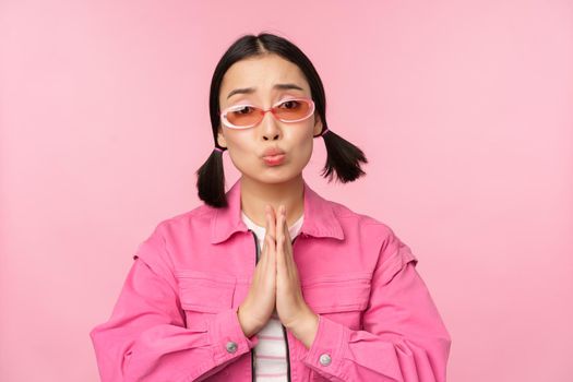 Please. Cute asian girl asking favour, begging, standing against studio background. Copy space