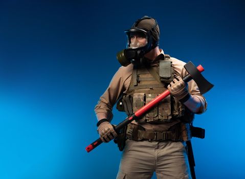 a soldier in military clothes with a bulletproof vest in a gas mask holds a red fire axe in his hands