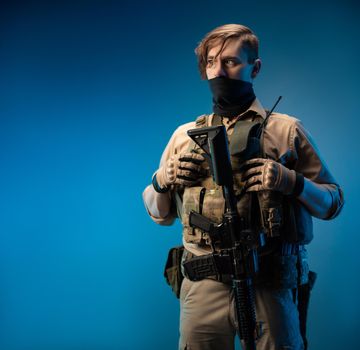 male special agent soldier in a bulletproof vest with an automatic rifle on a blue background