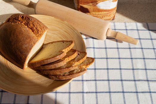 sliced home made fresh bread with crispy crust is in a wooden plate on a kitchen table