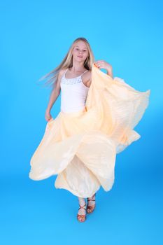 pretty teenage blond girl dancing in the yellow dress over the blue background