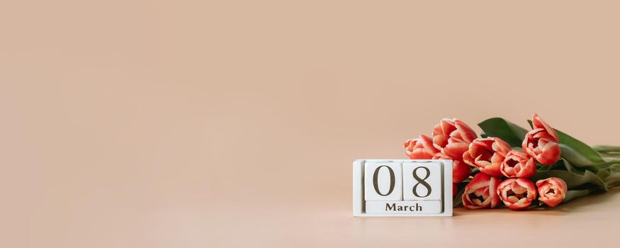 International women's day or eight march banner with copy space. 8 march date on perpetual calendar and bunch of red tulip on beige champagne background. Long horizontal banner