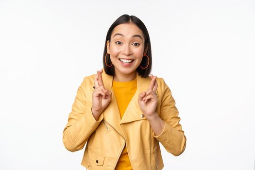 Portrait of excited asian woman looks hopeful, wishing, praying or begging, waiting for news, standing over white background, smiling enthusiastic.