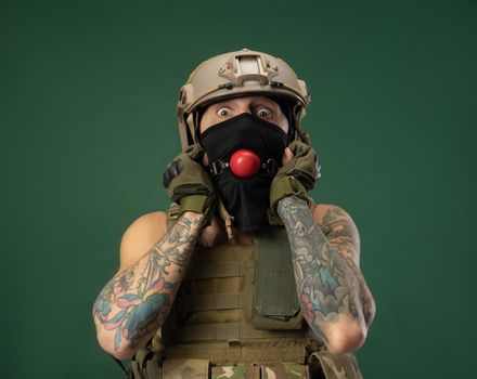 soldier man in military clothes helmet with a bdsm gag in his mouth expresses emotions, photo joke