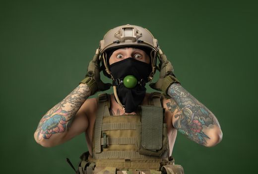 soldier man in military clothes helmet with a bdsm gag in his mouth expresses emotions, photo joke