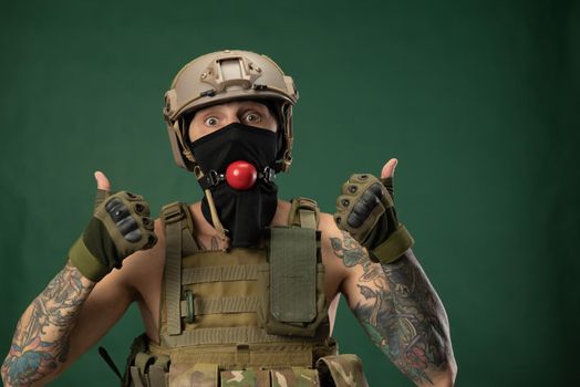 soldier man in military clothes helmet with a bdsm gag in his mouth expresses emotions, photo joke