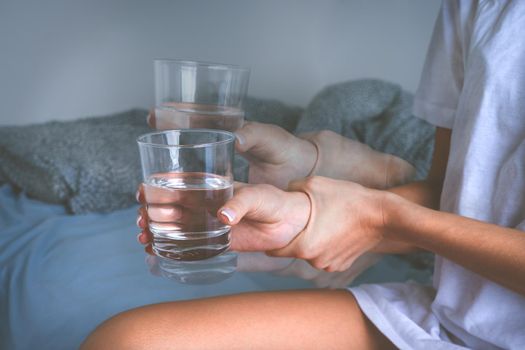 Woman holding glass of water in shaky hands and suffering from Parkinson's disease symptoms or essential tremor. High quality photo