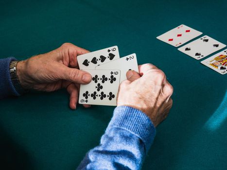 Grandfather's hands playing a card game. Playing cards on a green mat. At the table at home, with natural light from the window. Zenithal shot of hands