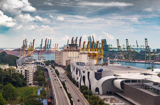 The huge busiest logistic port in Singapore, plenty of cranes to move containers, huge cargo ships in the background, shopping malls and skyscrapers surrounded by, entertainment island nearby. High quality photo