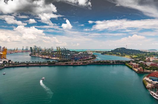 The huge busiest logistic port in Singapore, plenty of cranes to move containers, huge cargo ships in the background, shopping malls and skyscrapers surrounded by, entertainment island nearby. High quality photo