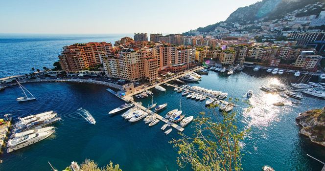 Panoramic image of Port Fontvieille - Monaco, top view from Monaco Ville, azur water, sun reflections on the water, harbour at sunny day, luxury apartments, a lot of yachts and boats, mountain. High quality photo