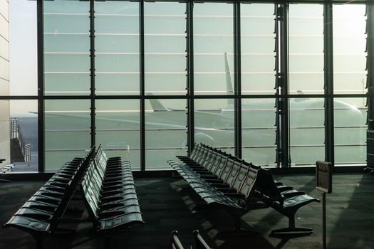 a deserted airport, empty benches by a panoramic window, a huge plane visible through the glass walls of an interchange hub in the United Arab Emirates. High quality photo
