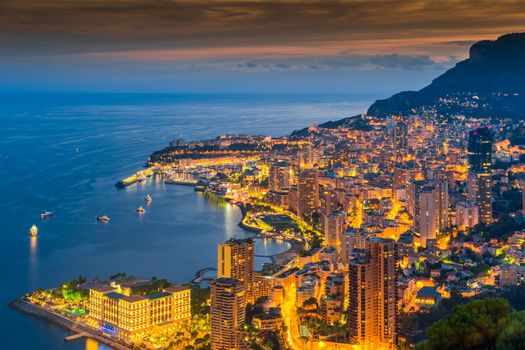 Aerial view of Monaco - Monte-Carlo at dusk, cityscape with night illumination, mountain, skyscrapers, mediterranean sea. High quality photo