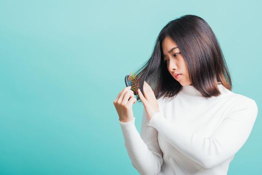 Young beautiful Asian woman upset with a comb and problem hair, Portrait female shocked suffering from hair loss problem, studio shot isolated on a blue background, medicine health concept