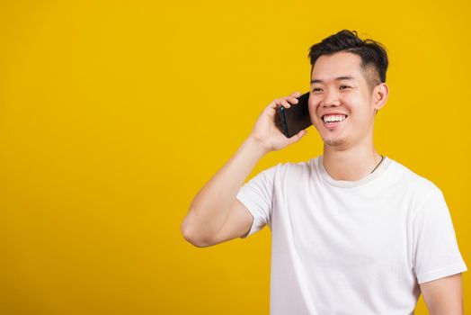 Asian handsome young man smiling positive talking on cellphone, lifestyle happy male using mobile smartphone studio shot isolated on yellow background