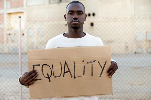 Young African American man looking at camera holding cardboard sign: Equality. Human rights activist. Demonstration concept.