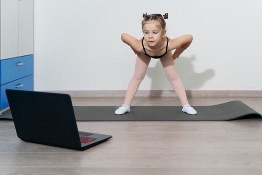 child girl in a gymnastic leotard is engaged in fitness with a trainer online.